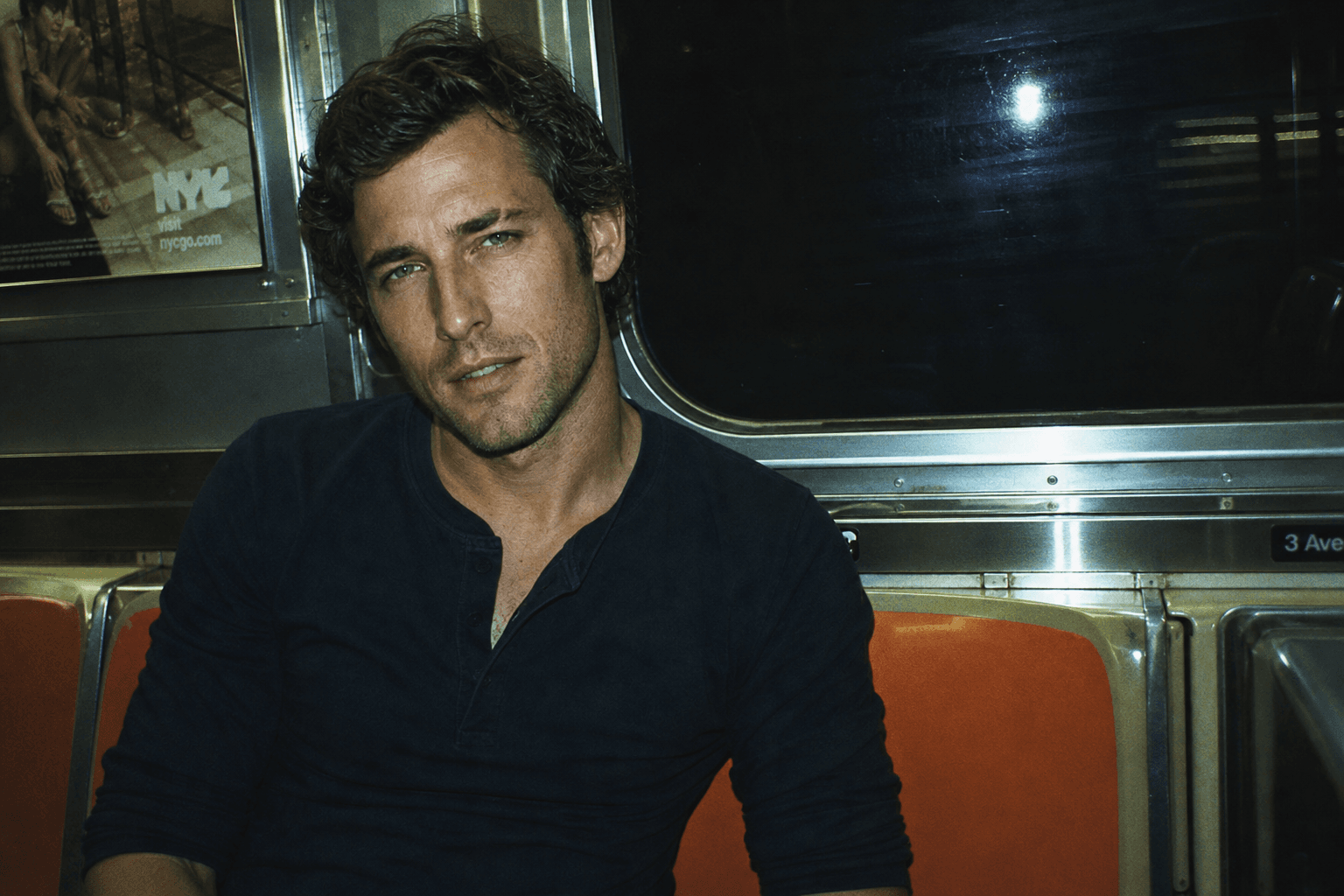 A younger Finn sitting alone on an orange New York subway seat at night, fluorescent light, film grain