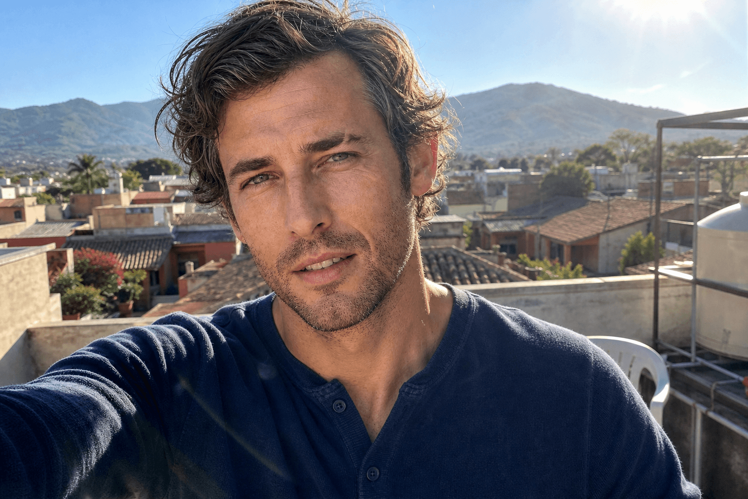 Finn on a rooftop in Oaxaca, navy henley, three-day stubble, mountains behind him