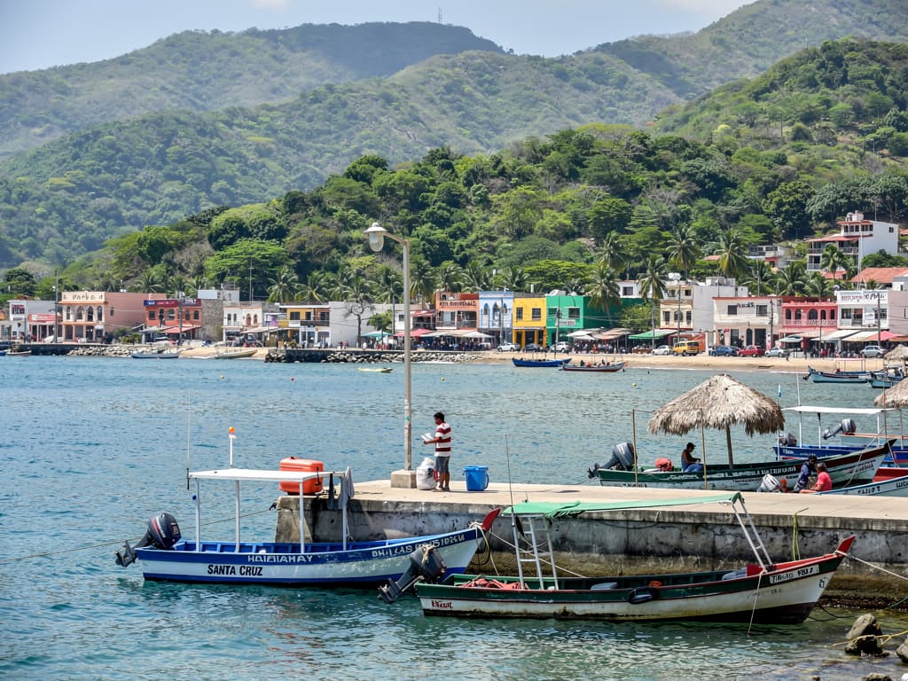 Santa Cruz bay in the midday glare, pangas tied near the pier, green hills behind